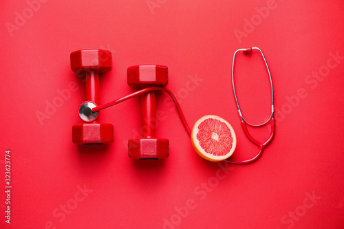 Stethoscope, grapefruit and dumbbells on color background