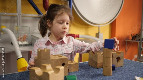 Little kid girl play wooden constructor assembles details of mind charging puzzle in playground room photo