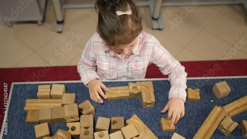 Little kid girl play wooden constructor assembles details of mind charging puzzle in playground room photo