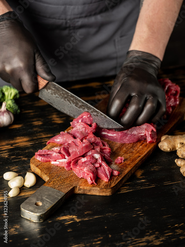 Cook cutting beef meat with big steel knife.