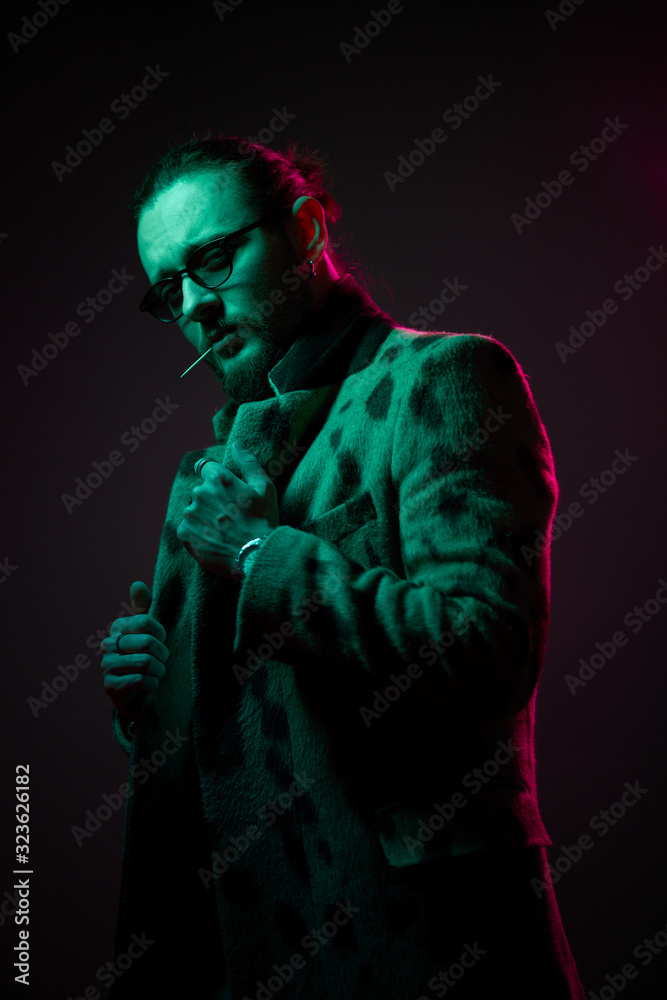 Guy with toothpick in his mouth, beard in glasses on black background