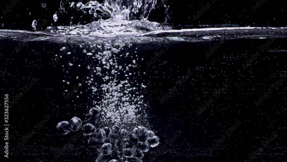 Bunch of grapes falling into water in slow motion. Isolated on black background. Close up view. Shot with cinema camera RED Dragon, UHD, 240fps.