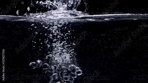 Bunch of grapes falling into water in slow motion. Isolated on black background. Close up view. Shot with cinema camera RED Dragon, UHD, 240fps.