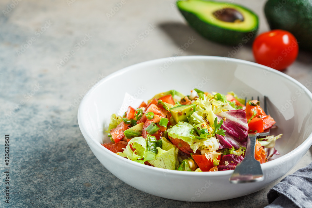 Avocado and tomato salad in white bowl. Vegan food concept.