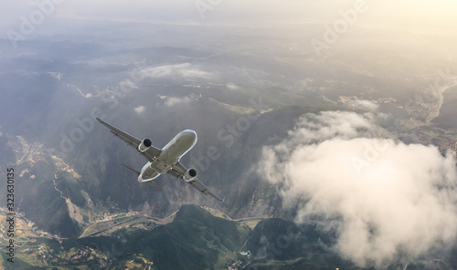 Airplane flying at high altitude over green mountains and sky at sunrise