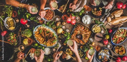 Flat-lay of family celebrating over rustic table with Turkish cuisine lamb chops, quince, green bean, vegetable salad, babaganush, rice pilav, pumpkin dessert, lemonade, top view. Middle East cuisine