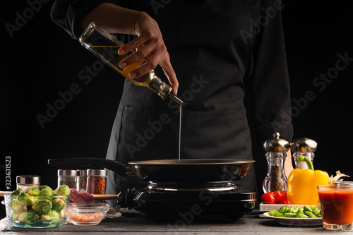 Cooking, the chef pours oil in a pan, against the background of vegetables. Cooking. Recipe book, cooking and gastronomy.