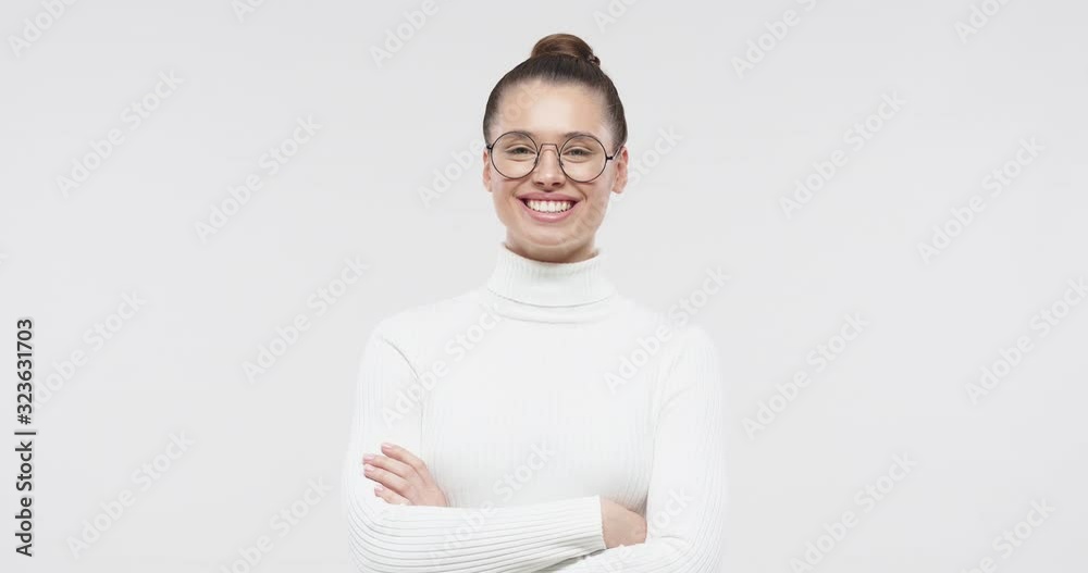 Woman crossed arms. Portrait of young smiling girl standing in white sweater and round eyeglasses, isolated on studio gray background Woman crossed arms. Portrait of young smiling girl standing in white sweater and round eyeglasses, isolated on studio gray background