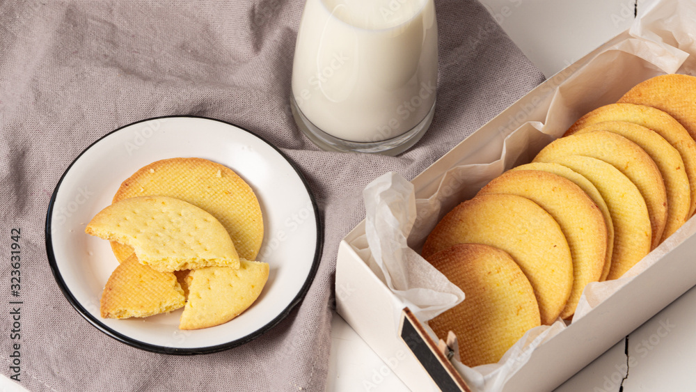 Few crashed cookies on a plate. There is a jar of milk near it. Also there is a box with homemade cookies in it. Grey napkin, white wooden table. Few crashed cookies on a plate. There is a jar of milk near it. Also there is a box with homemade cookies in it. Grey napkin, white wooden table.