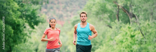 Running couple on trail run in forest park banner panoramic header. Fit athletes runners man and woman training partners friends jogging together in summer outdoors.