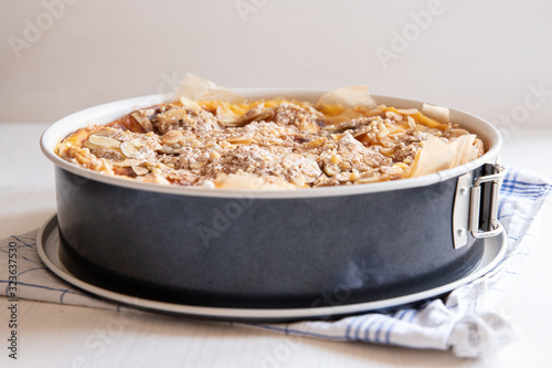 ganzer Bratapfelkuchen in einer Backform auf hellem weißen Holzgrund mit Küchentuch photo