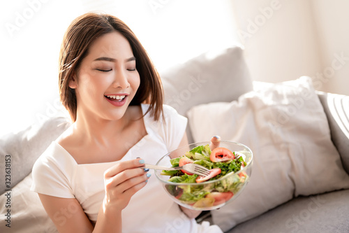 Healthy asian woman eating salad in her living room. Clean food salad eating concept.