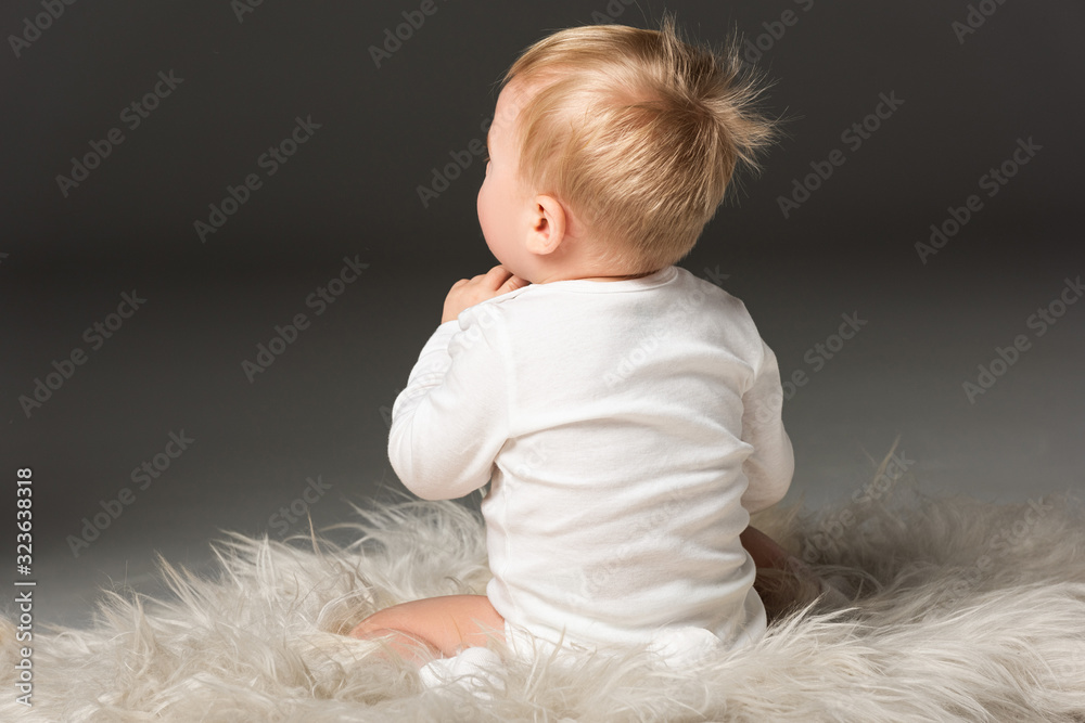 Back view of cute kid sitting on fur on isolated on black Back view of cute kid sitting on fur on isolated on black