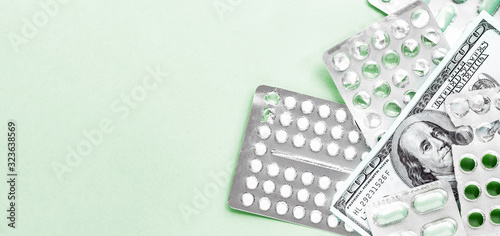 white and green pills in blister with money on a green background, medicine flat lay with copy space, rising cost of health care