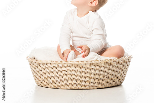 Cropped view of cute child looking up and sitting on blanket in basket on white background