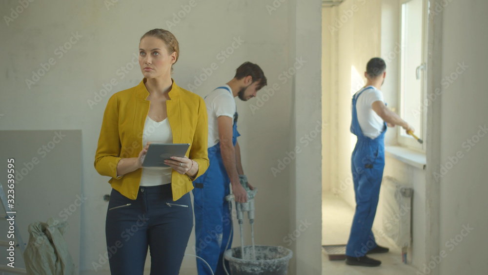 Obraz premium Woman walks with tablet, repairmen work in the flat
