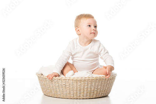 Cute child looking away and sitting on blanket in basket on white background