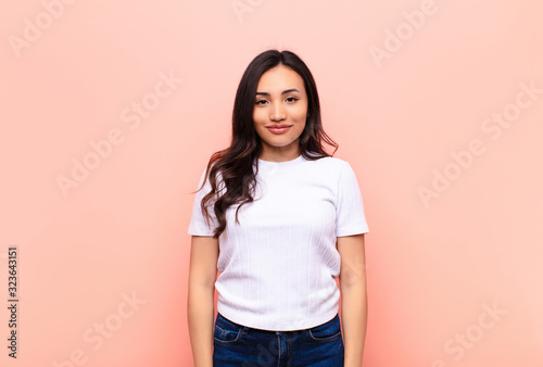 young latin pretty woman smiling positively and confidently, looking satisfied, friendly and happy against flat wall