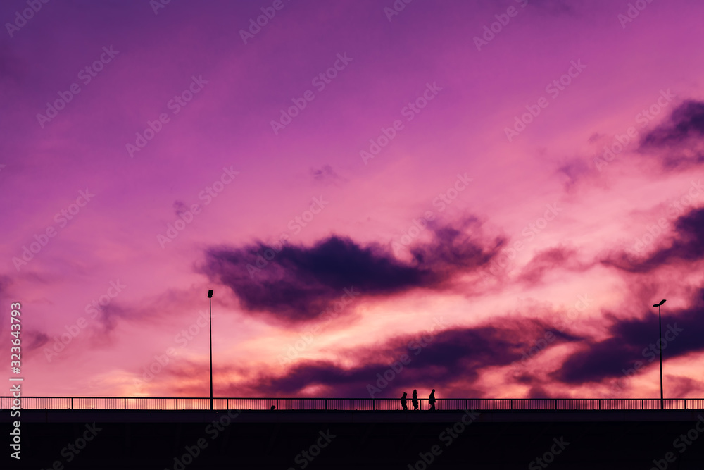 Fototapeta premium Silhouettes of three young people crossing the bridge in sunset