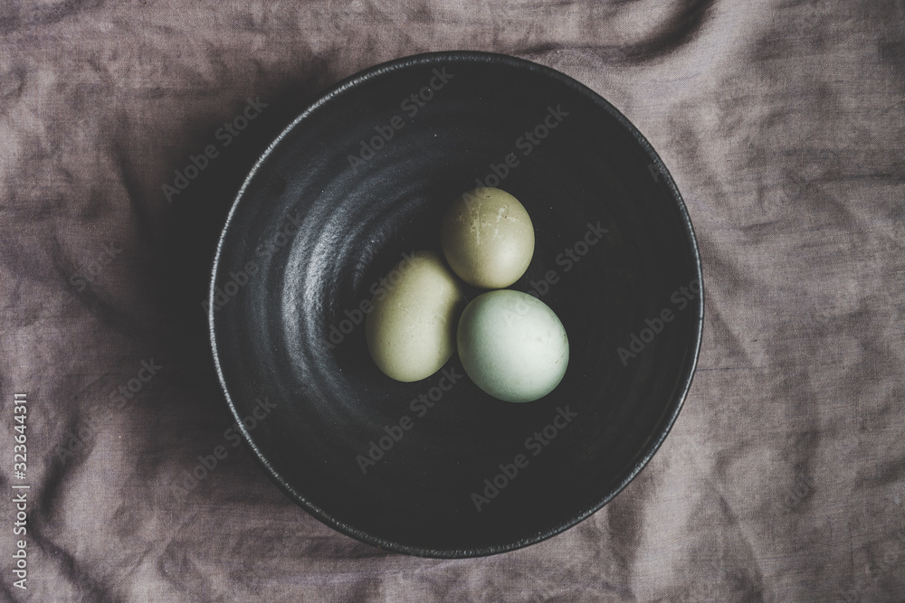 Obraz premium organic eggs in black ceramic bowl moody flat lay indoor photo