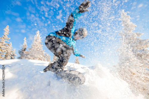 Active man snowboarder riding on slope during sunny day in mountains. Dust snow forest