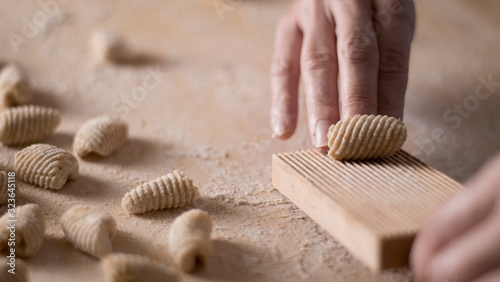 Close up process of homemade vegan gnocchi pasta with wholemeal flour making. The home cook crawls on the special wooden tool the gnocco , traditional Italian pasta, woman cooks food in the kitchen photo