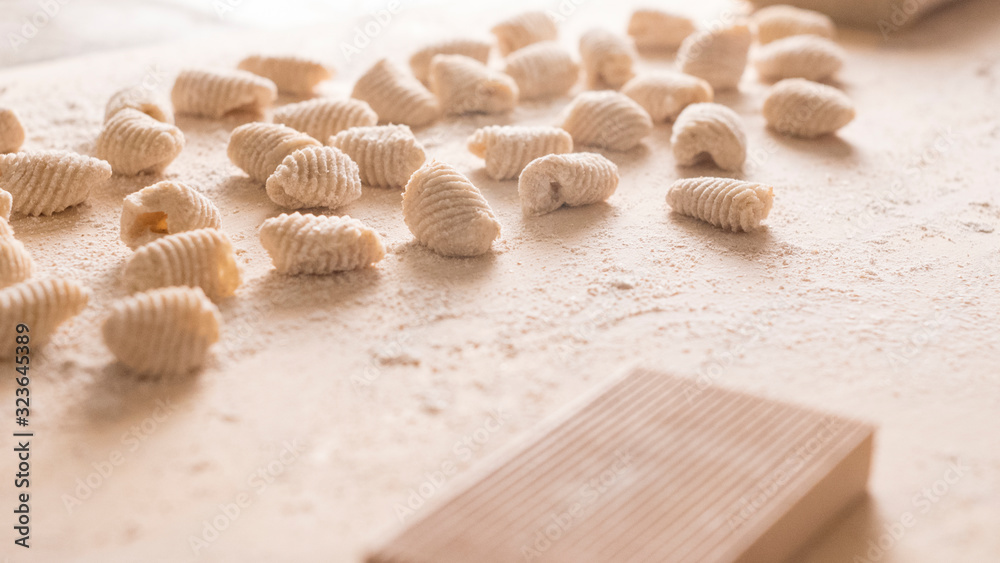 Close up of homemade vegan gnocchi pasta with wholemeal flour on the wooden chopping board with back light morning sunlight bokeh effect, traditional Italian pasta