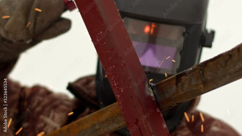 A man in a protective mask is welding a metal structure. View from the side of the structure A man in a protective mask is welding a metal structure. View from the side of the structure