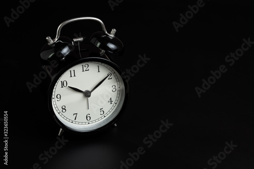 Black retro alarm clock in dark black bedroom with copy space using as sleeping time, clock of life, time passing or wake up concept