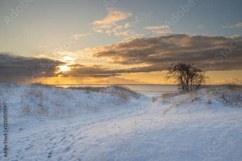 Sunrise light breaking through the clouds over the snowy beach of Baltic sea in winter morning