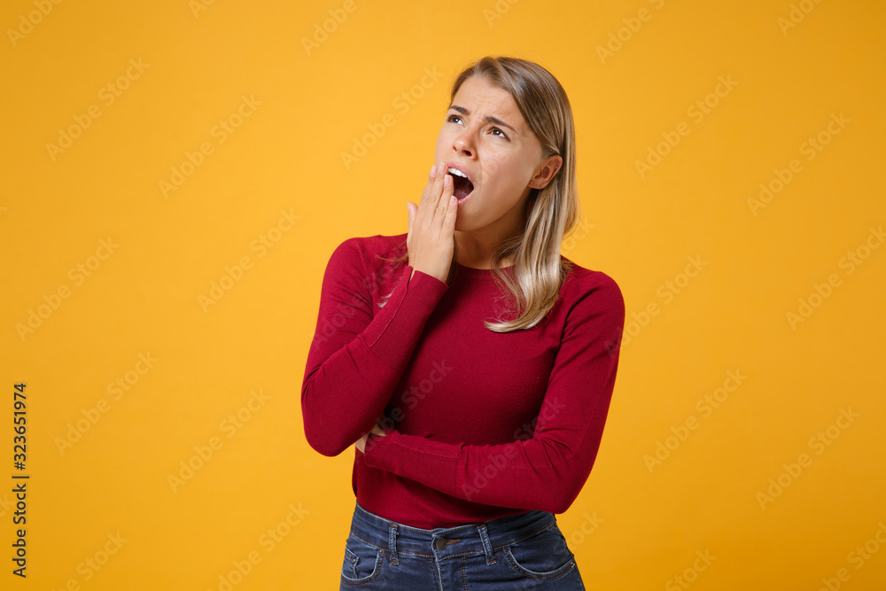 Boring tired young blonde woman in casual clothes posing isolated on yellow orange wall background in studio. People emotions lifestyle concept. Mock up copy space. Yawning, covering mouth with hand.