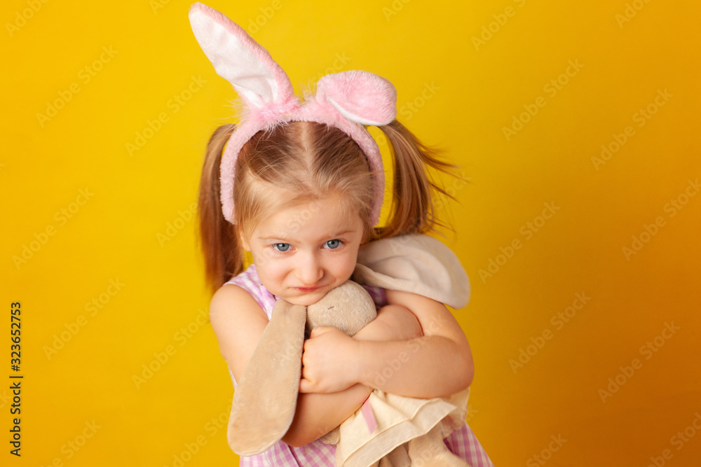 Little girl holding her bunny toy against yellow background Little girl holding her bunny toy against yellow background