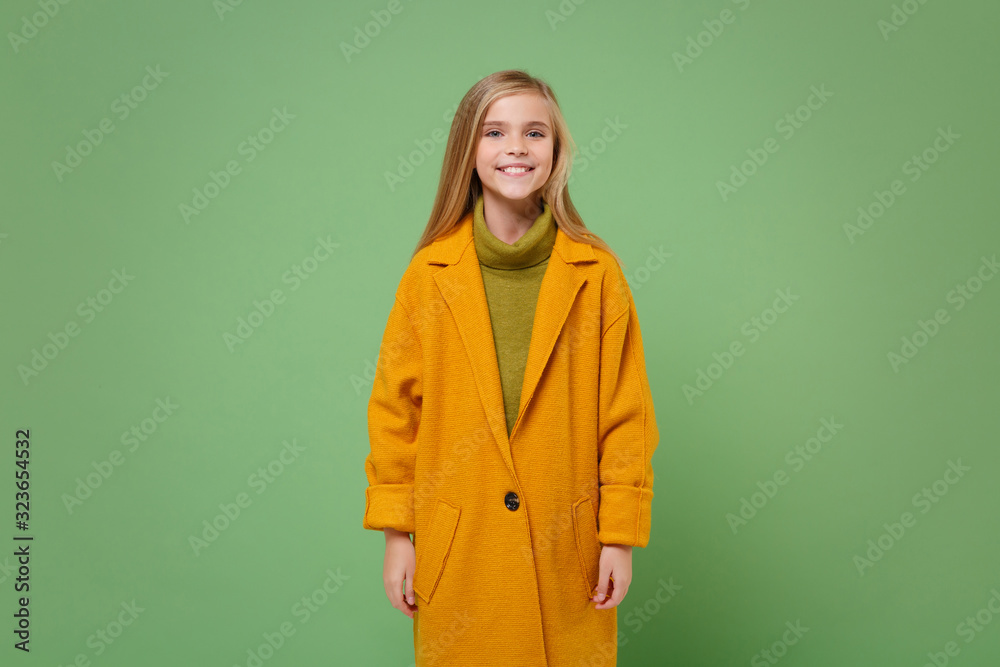 Smiling little blonde kid girl 12-13 years old in yellow coat posing isolated on pastel green wall background children studio portrait. Childhood lifestyle concept. Mock up copy space. Looking camera. Smiling little blonde kid girl 12-13 years old in yellow coat posing isolated on pastel green wall background children studio portrait. Childhood lifestyle concept. Mock up copy space. Looking camera.