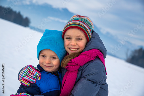 Girl hugging her little brother in the snow