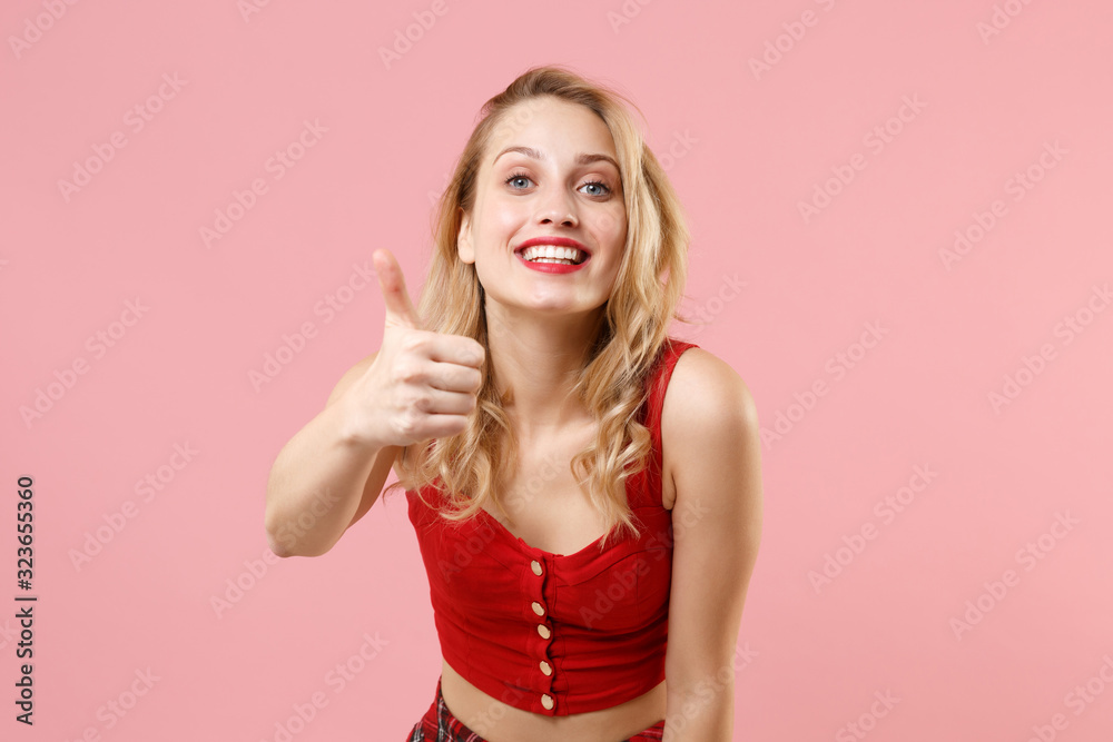 Smiling attractive young woman girl in red sexy clothes posing isolated on pastel pink wall background studio portrait. People sincere emotions lifestyle concept. Mock up copy space. Showing thumb up. Smiling attractive young woman girl in red sexy clothes posing isolated on pastel pink wall background studio portrait. People sincere emotions lifestyle concept. Mock up copy space. Showing thumb up.