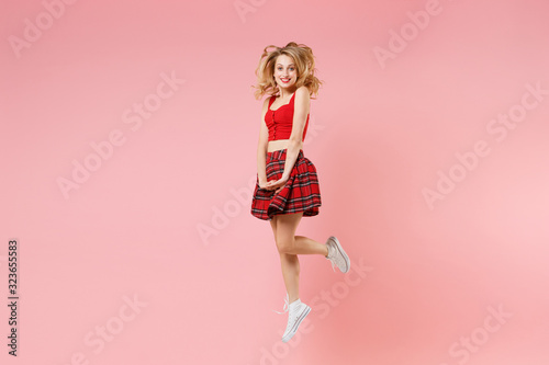 Smiling young blonde woman girl in red sexy clothes posing isolated on pastel pink background studio portrait. People sincere emotions lifestyle concept. Mock up copy space. Jumping, looking camera.