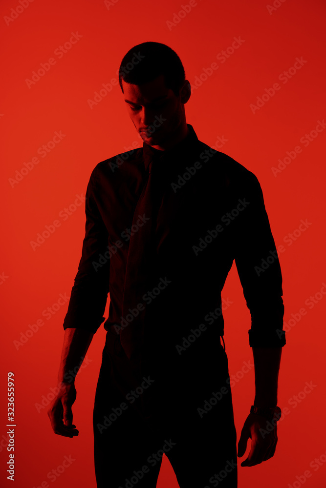 Silhouette of a young confident handsome businessman wearing black shirt in red light