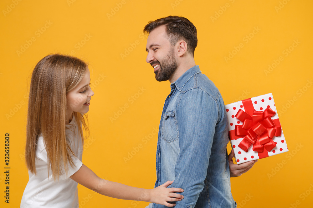 Obraz premium Side view of cheerful bearded man with child baby girl. Father little kid daughter isolated on yellow background. Love family day parenthood childhood concept. Hold present box with gift ribbon bow.
