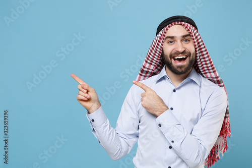 Canvas Print Cheerful young bearded arabian muslim man in keffiyeh kafiya ring igal agal casual clothes isolated on pastel blue wall background
