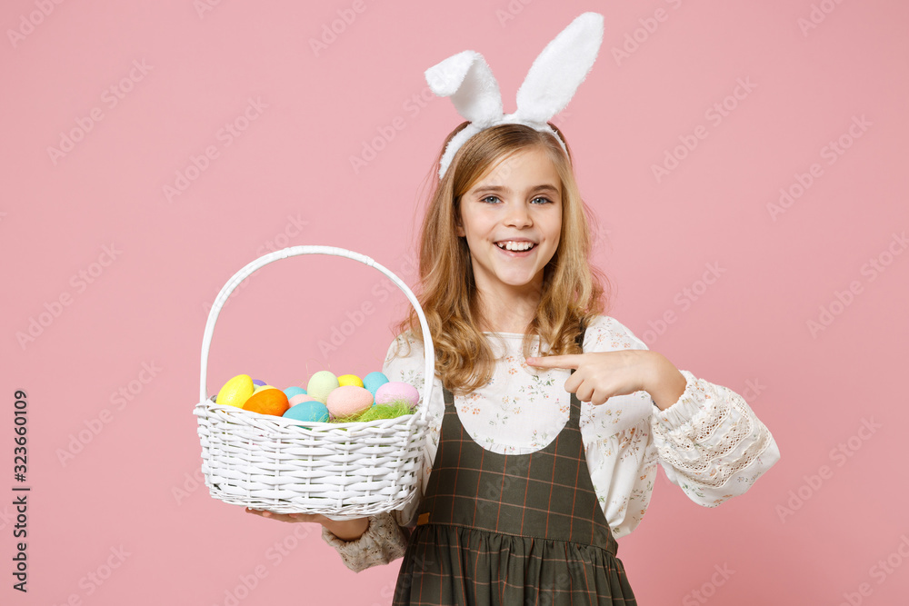 Little pretty blonde kid girl 11-12 years old in spring dress, bunny rabbit ears hold in hand wicker basket colorful eggs isolated on pastel pink background. Childhood lifestyle Happy Easter concept. Little pretty blonde kid girl 11-12 years old in spring dress, bunny rabbit ears hold in hand wicker basket colorful eggs isolated on pastel pink background. Childhood lifestyle Happy Easter concept.