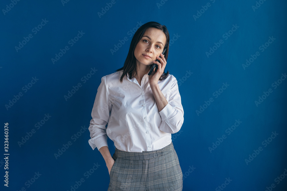 Woman standing near wall talking on mobile phone looking at camera