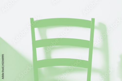 Wooden chair on wall background. The back of the chair, detail. Minimal style, minimalism. Green toned photo