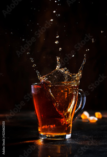 Splash in glass cup of black tea with natural steam on brown background