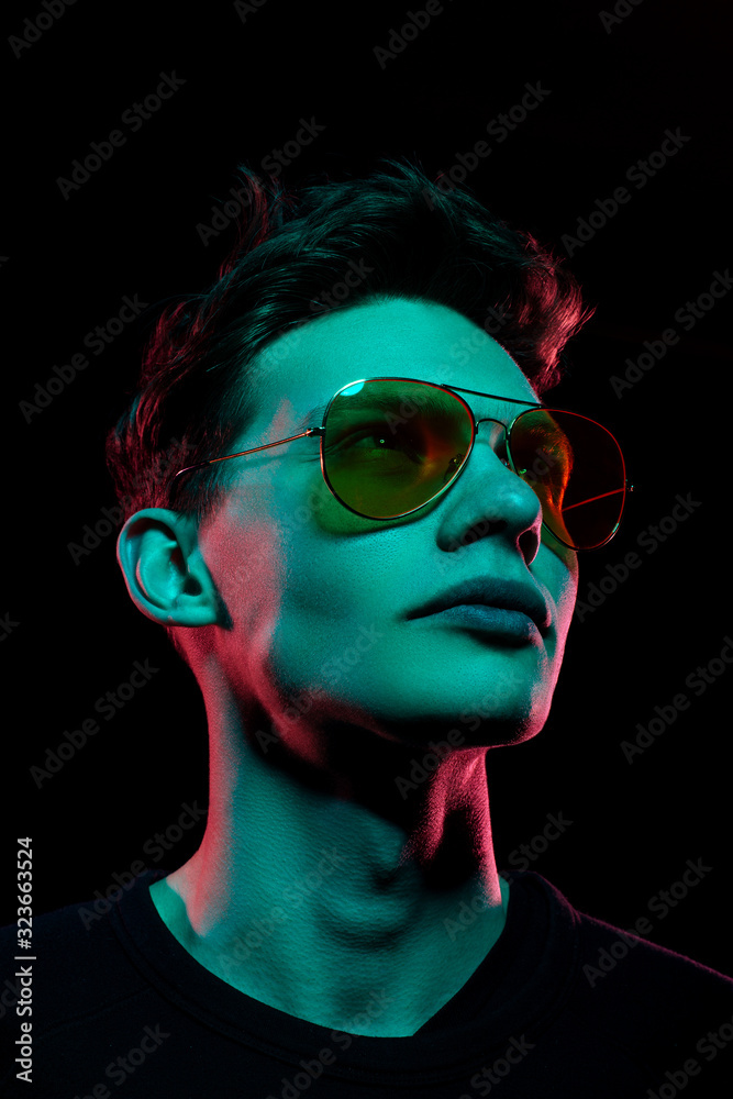 Portrait of a fashion trend male model neon gel light in studio on a dark black background