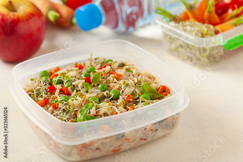 Trendy lunch with rice and vegetables. Served in a portable box on a bright painted background. Perfect for work or school. Front view.