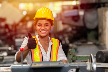 Girl teen worker with safety helmet show thumb up working as labor in industry factory with steel machine.
