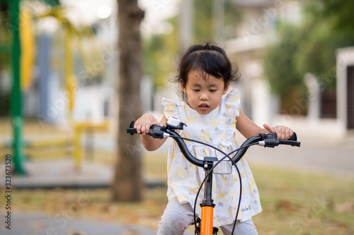 Yellow dressed beautiful little girl riding bicycle at park.