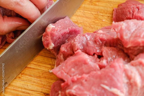 Closeup of the hands of a butcher cutting slices of raw meat off a large loin