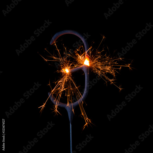 Burning sparkler in shape of number three, digit 3, isolated on black background.