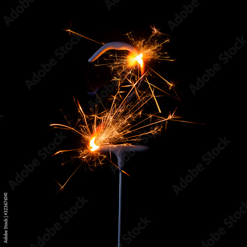 Burning sparkler in shape of number two, digit 2, isolated on black background.